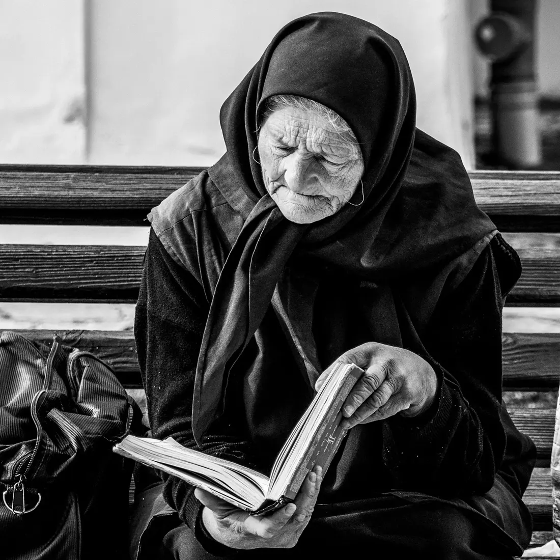 Fotografía en blanco y negro de una mujer mayor leyendo un libro en un banco