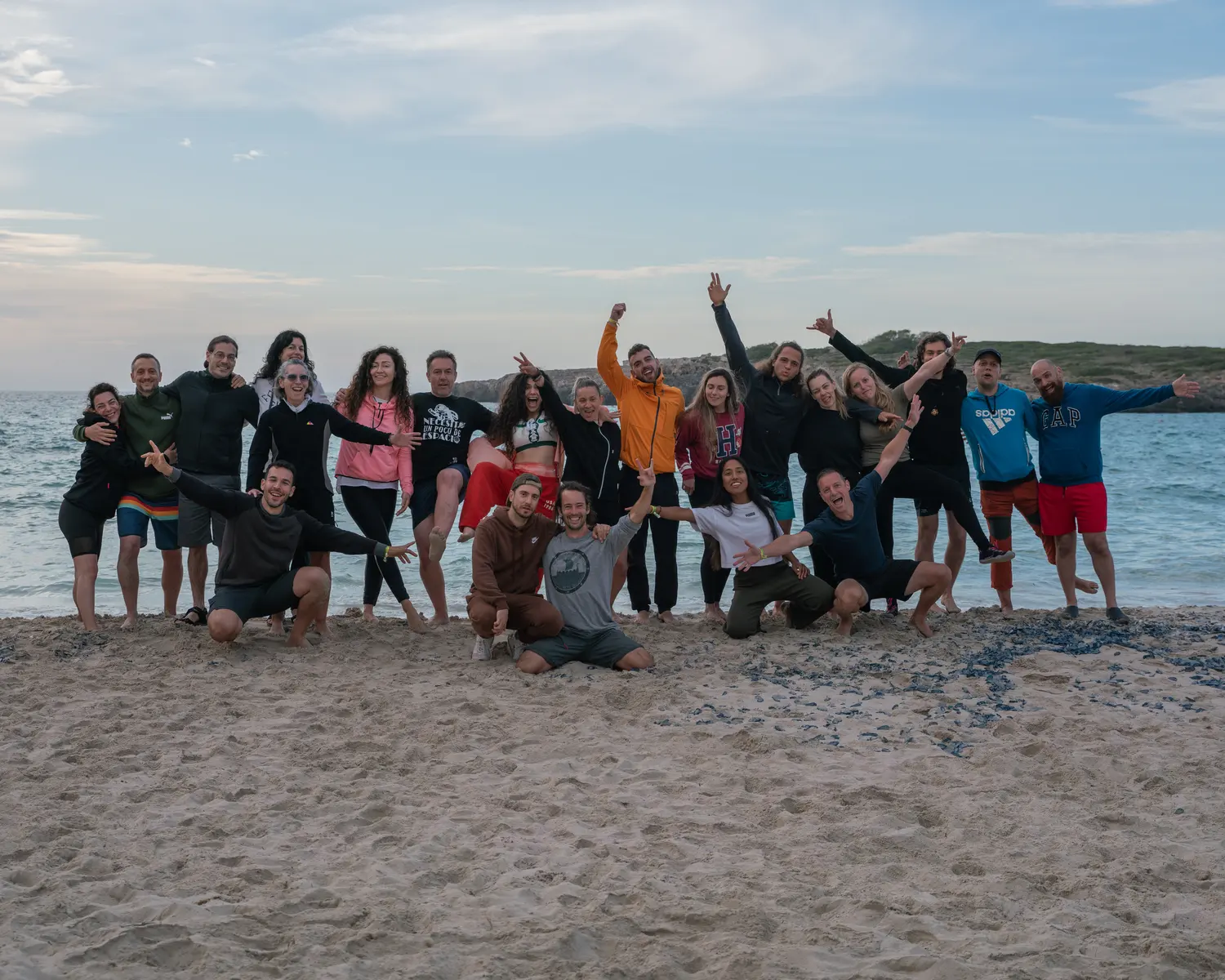 Foto de grupo en una playa de Mallorca al atardecer, con más de veinte participantes de un retiro celebrando