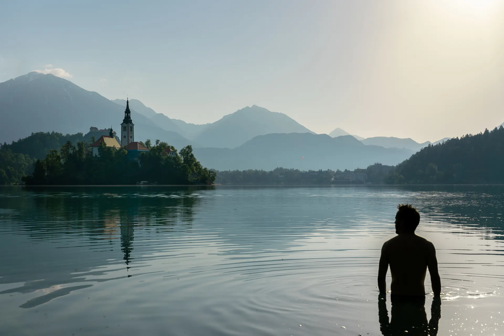 Miguel entrando al amanecer en las aguas quietas del lago de Bled, en Eslovenia, con la isla y las montañas al fondo