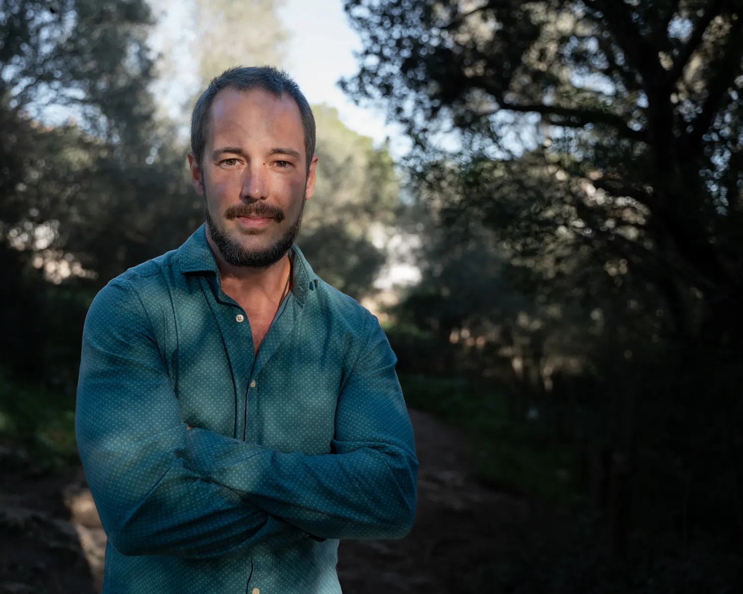 Retrato de Miguel Frontera entre encinas, con la luz del atardecer filtrándose entre los árboles