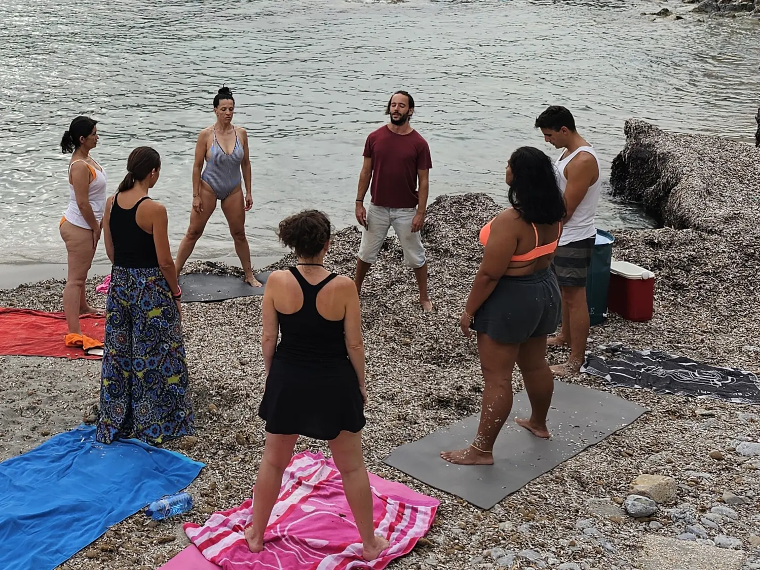 Miguel guiando una sesión de breathwork en círculo, de pie sobre esterillas en una cala de Mallorca
